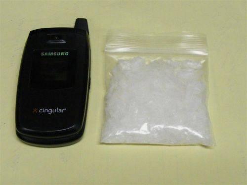 A bag full of a white substance next to an older flip style phone.