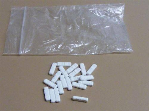 Several long white pills next to a clear bag.