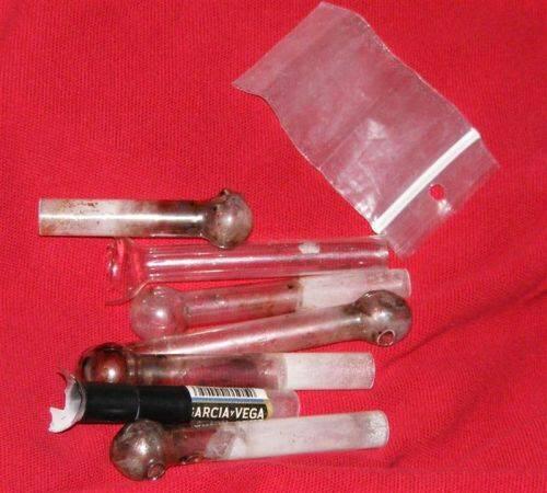 Seven pipes next to a small bag, several are broken, and several have a powdery substance on them.
