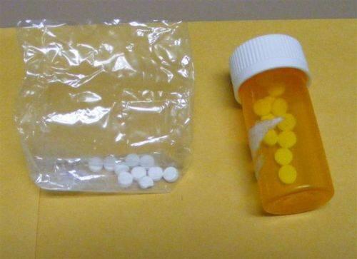 Several pills in a small bag next to a prescription bottle with more pills inside.