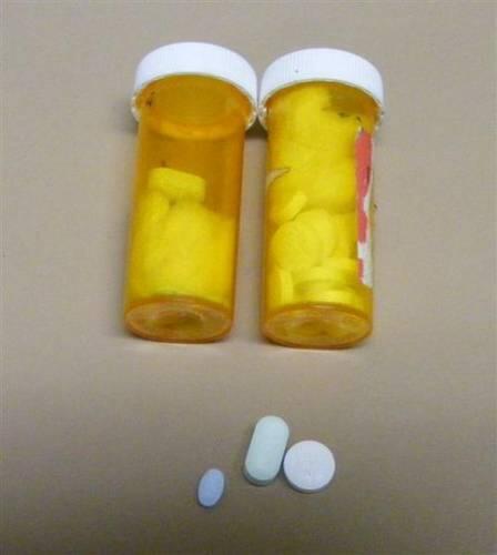 Two prescription medication bottles filled with pills with three more pills below them.